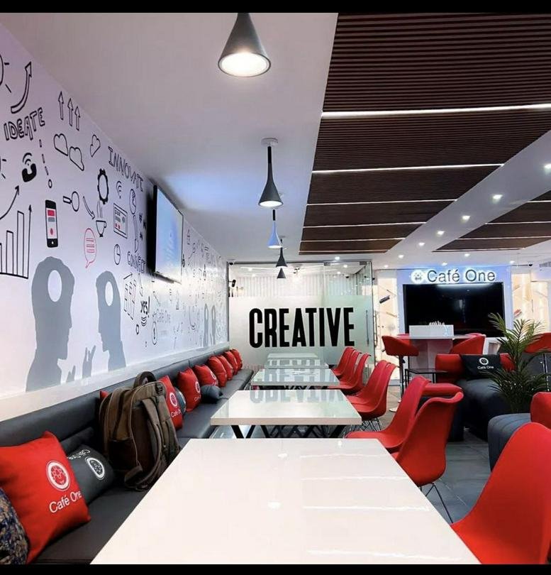 Spacious coworking lounge at E-Centre, 3rd Floor, 1-11 Commercial Avenue with red chairs and creative wall art.