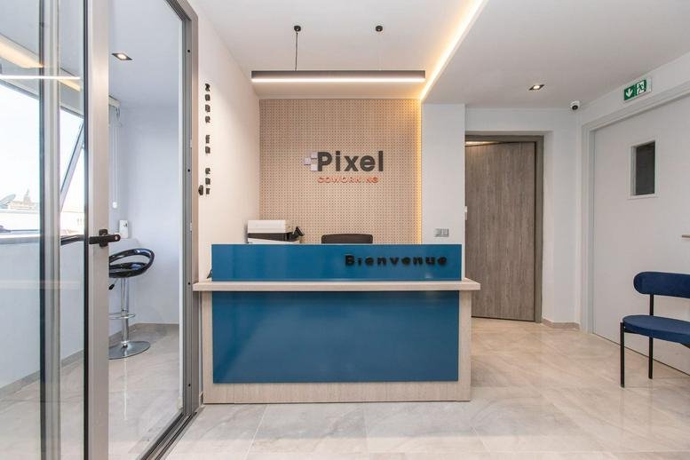 The reception area of Pixel Coworking featuring a blue front desk against a light wood-paneled wall.