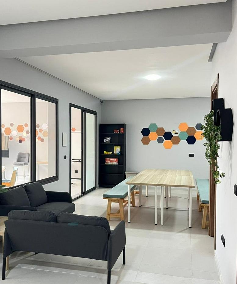 Spacious communal lounge at Hive Collab, Espace Bureaux Mariya with wooden tables and dark sofas.