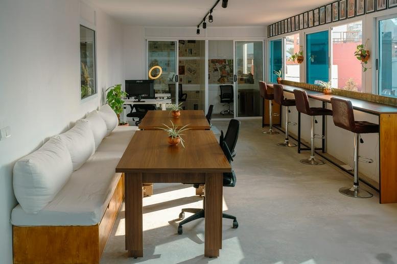 Spacious coworking area with long wooden tables and a cushioned bench seat.