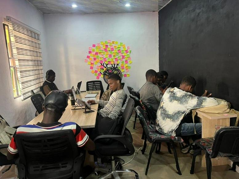 Coworking space at Pracvarsity, Sam Guobadia Street featuring people at desks and a wall decorated with sticky notes.
