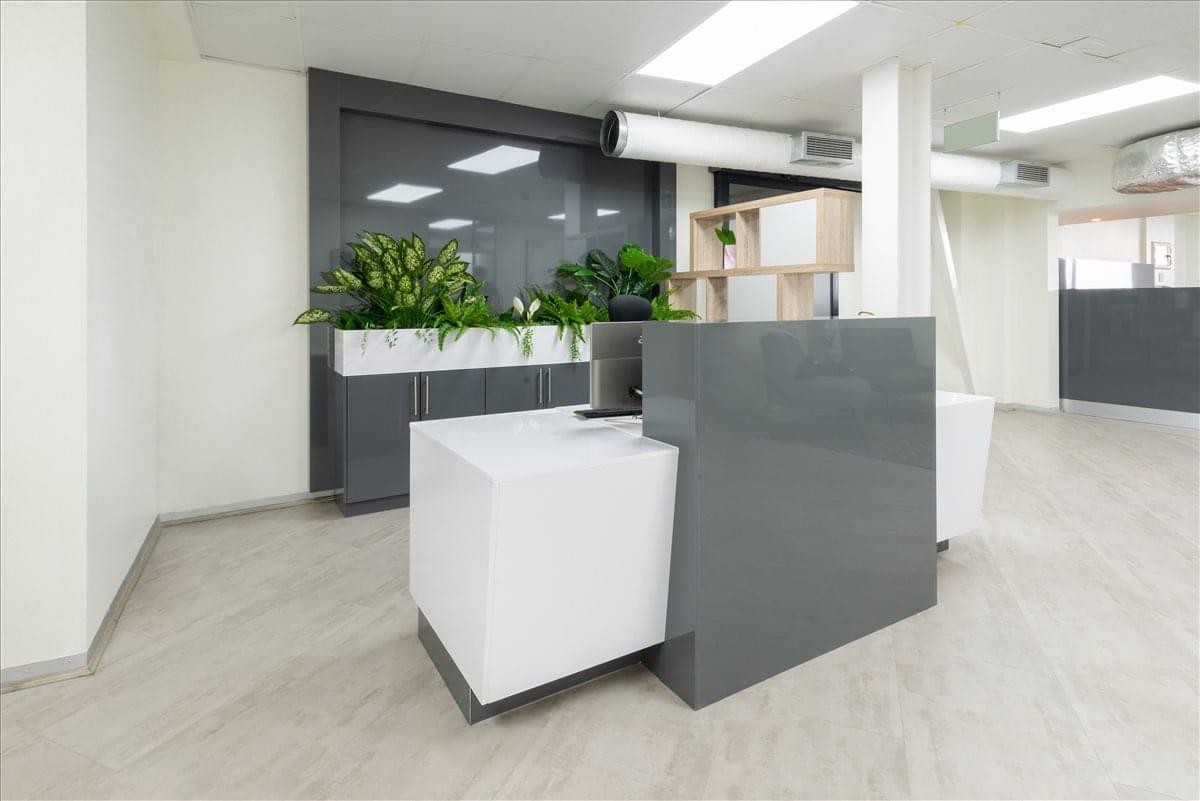 The sleek, modern reception area at Ingenuity Park featuring a minimalist grey and white desk with indoor plants.