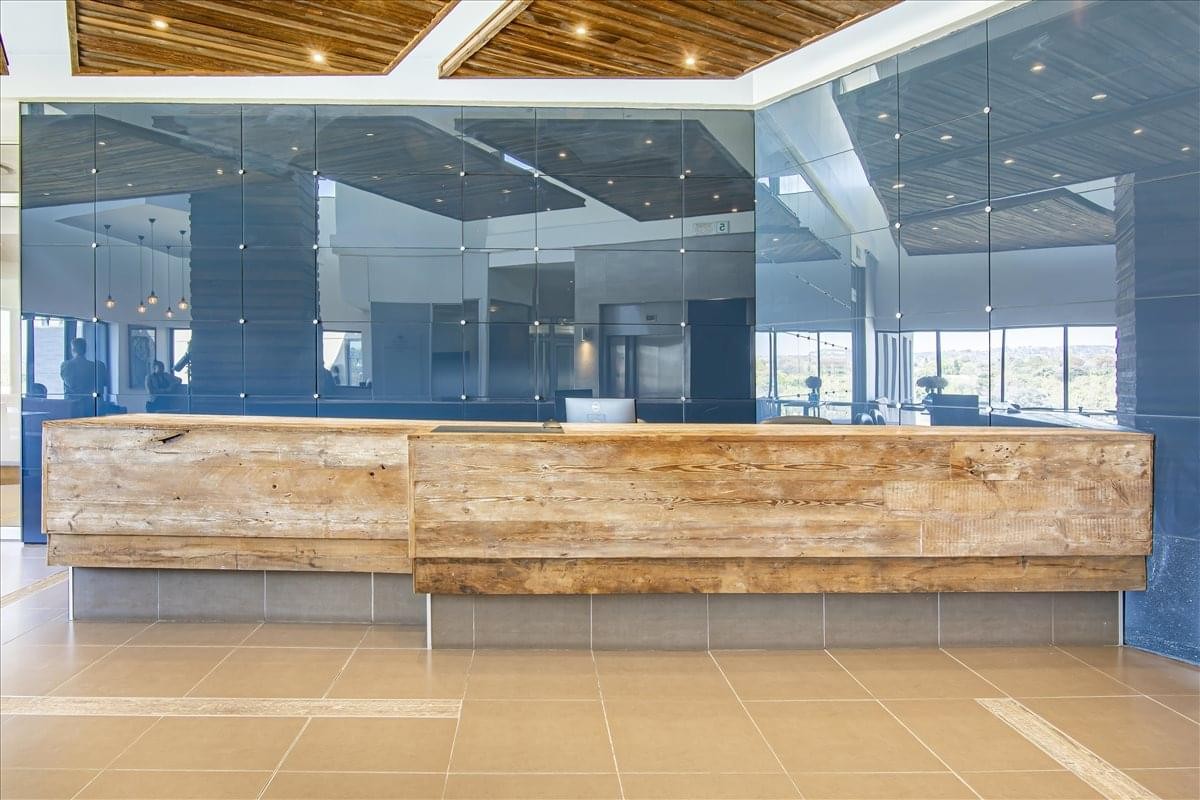 Spacious reception desk made of reclaimed wood against a dark glass feature wall at Bloukrans Building.