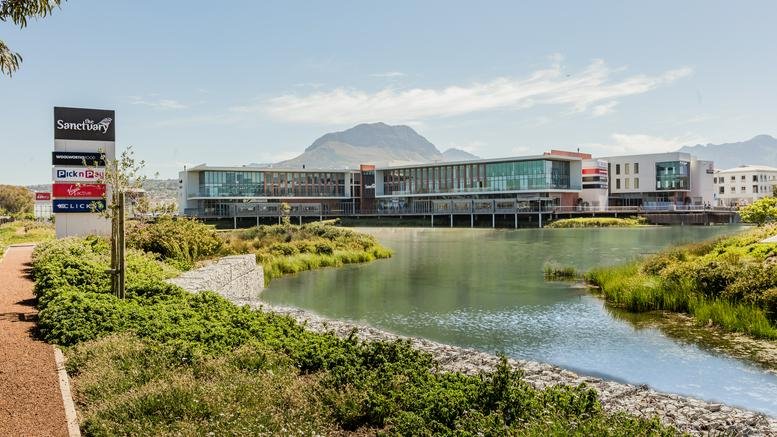 Exterior view of The Sanctuary Mall building overlooking a scenic lake and mountains in Somerset West.