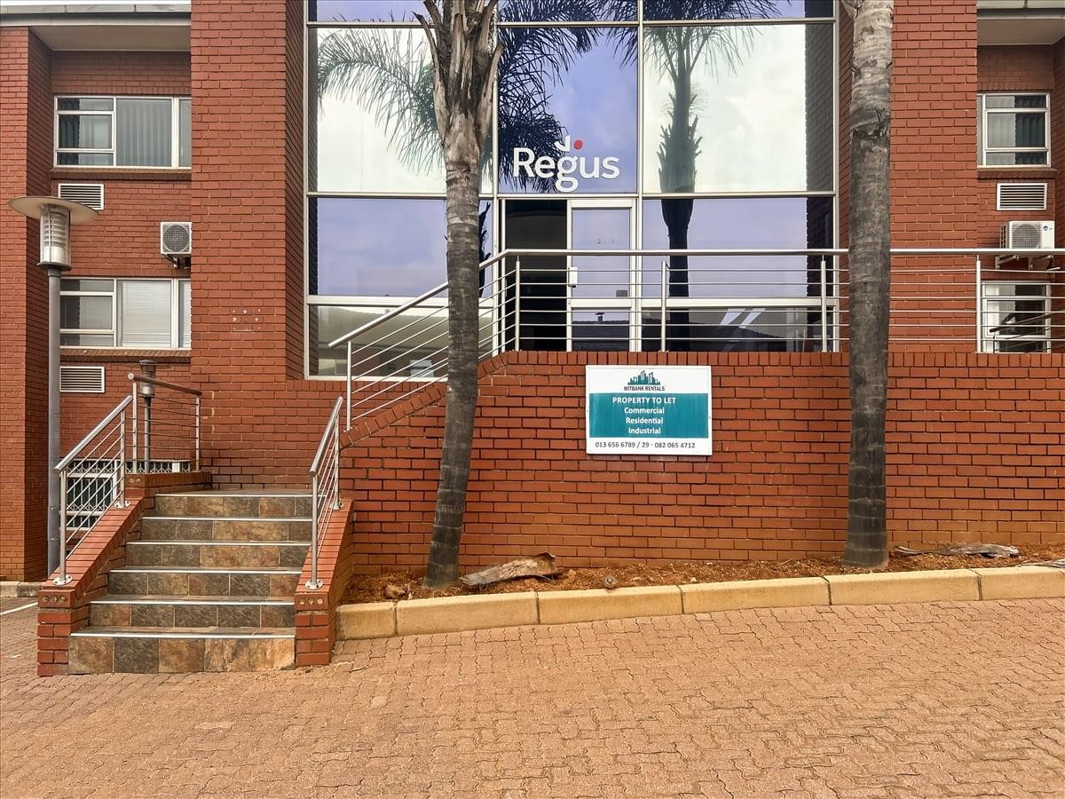 Exterior brick facade of the Witbank Building with a glass entrance and palm trees.