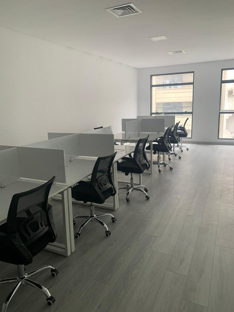 Open-plan office with white desks and black ergonomic chairs.