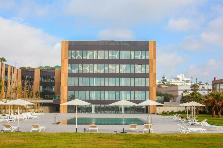Exterior view of the modern glass-facade Anfa Place, Immeuble Most with a poolside lounge area.