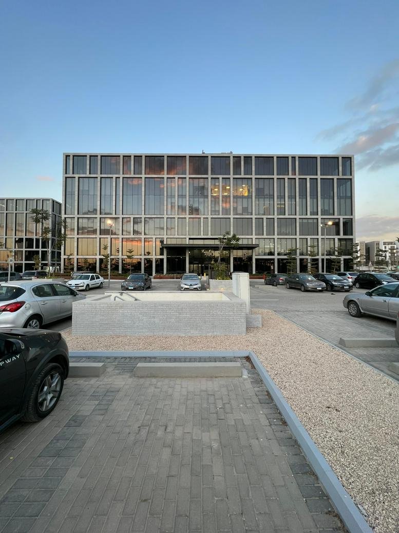 Wide view of the glass-walled office building from a paved parking area.