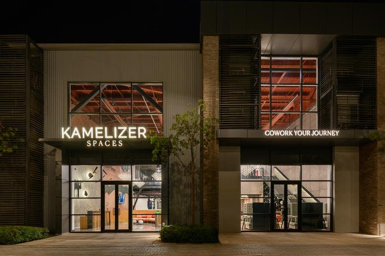 Evening exterior of Kamelizer Spaces at District 5, Ain El Sokhna Road, featuring glowing signage and glass doors.