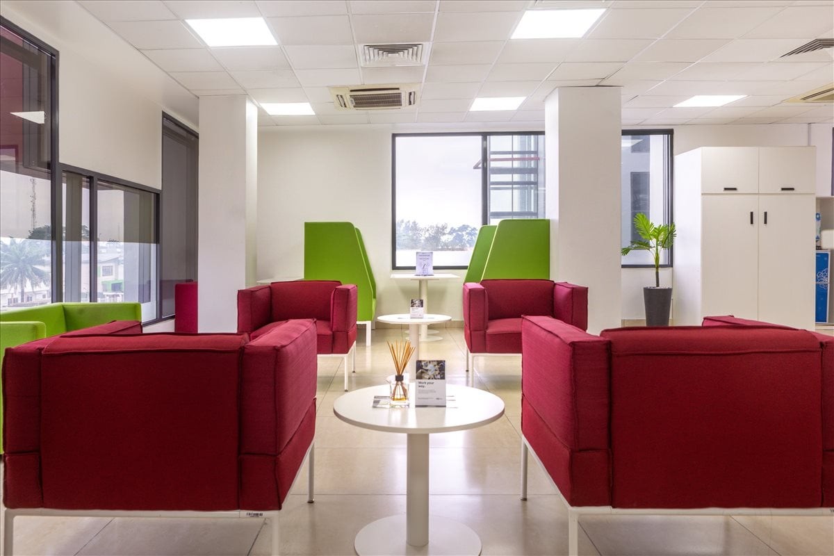 Spacious communal lounge area with vibrant red armchairs, green booth seating, and round white tables.