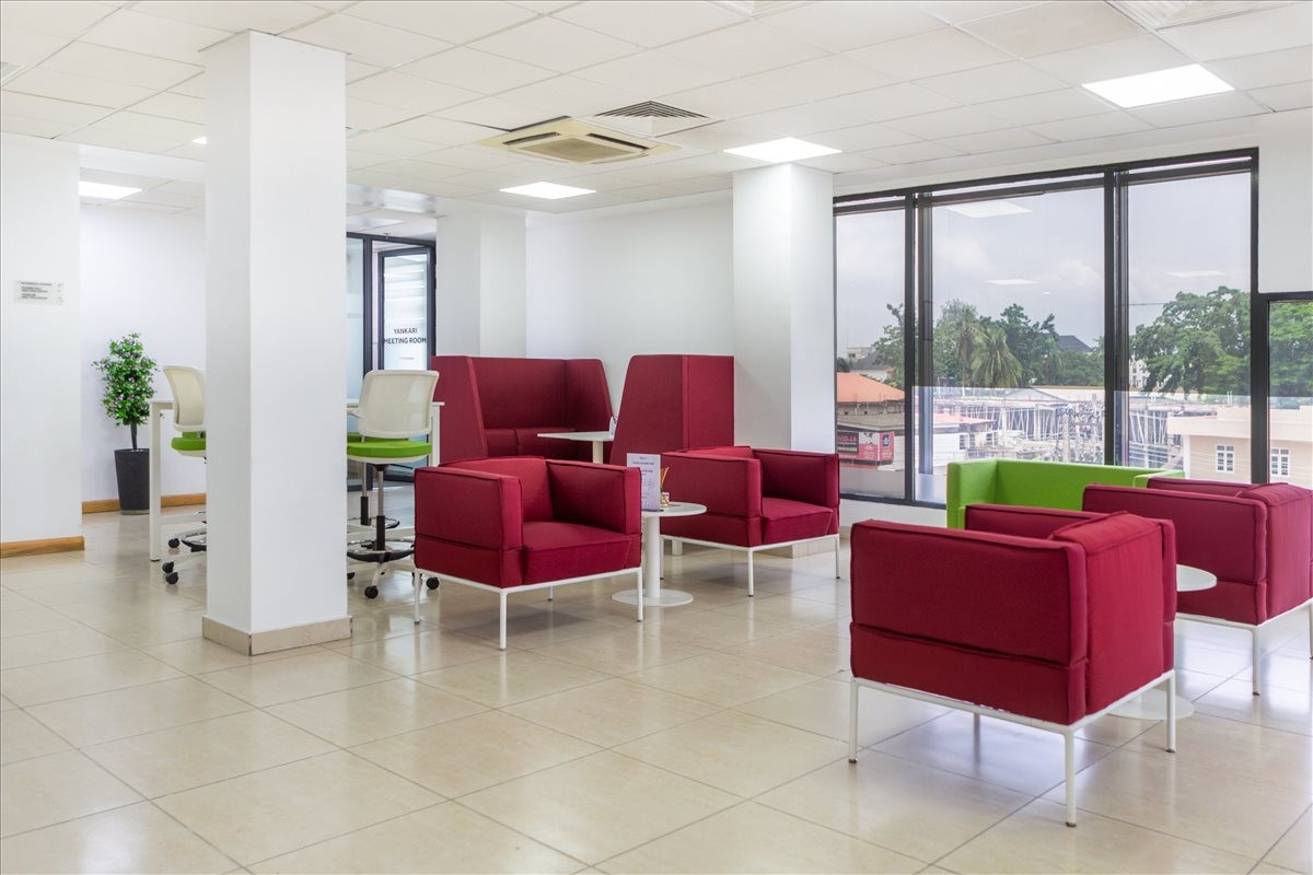 Large open coworking area with red upholstered armchairs, white columns, and floor-to-ceiling windows.
