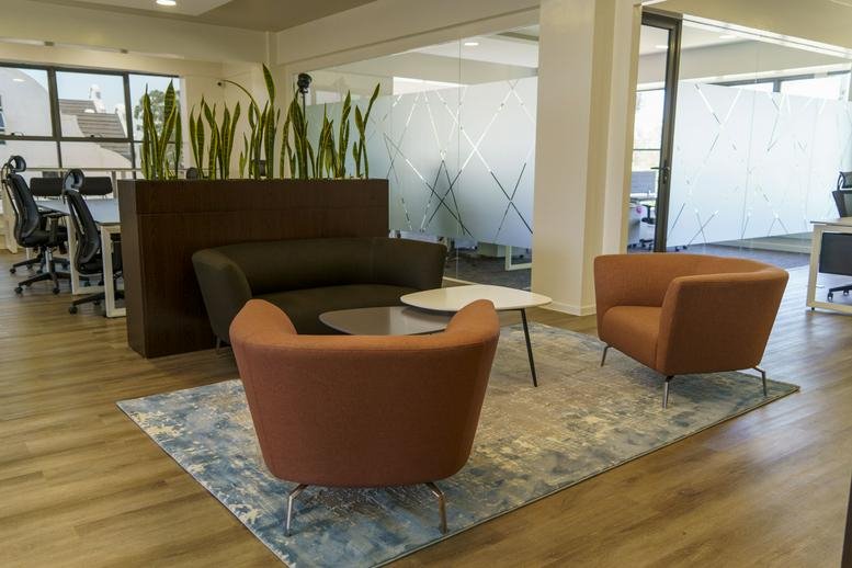 Spacious lounge at Millennium Business Park featuring modern orange armchairs and a grey area rug.