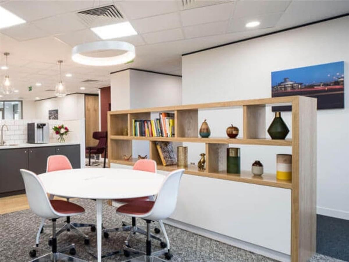 Communal breakout area with a round white table, pink chairs, and a decorative wooden bookshelf.