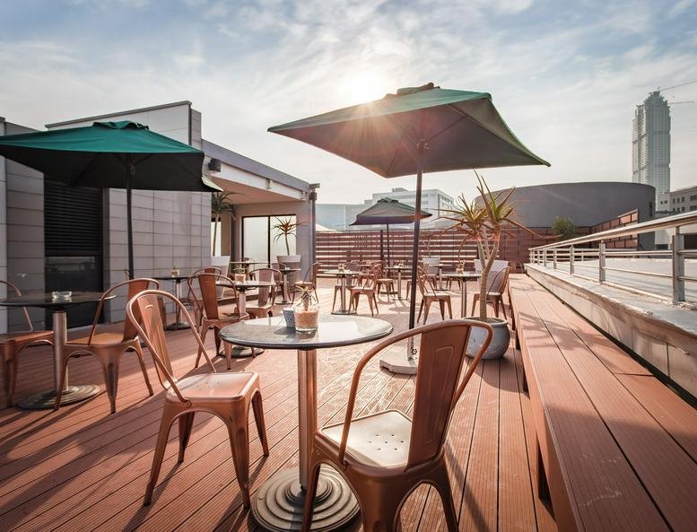 Wooden rooftop terrace with green umbrellas and city views.
