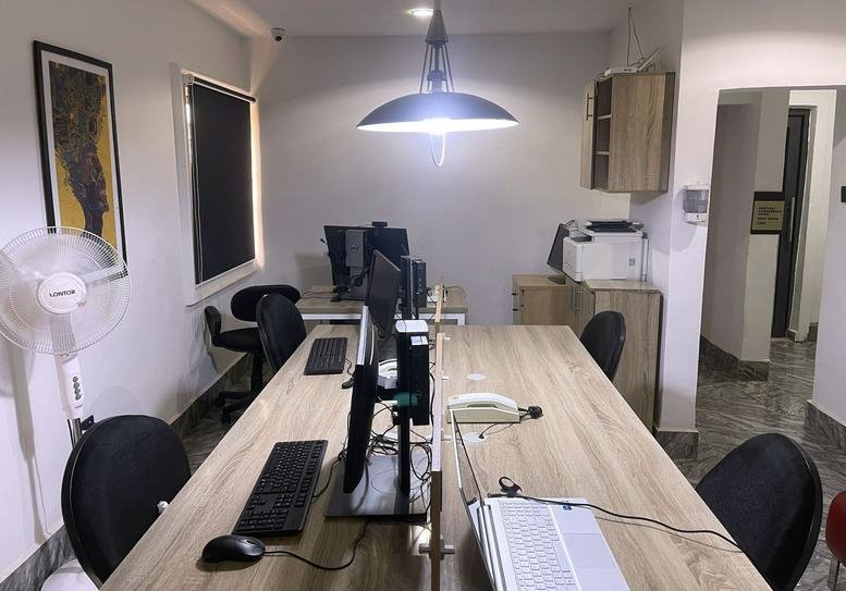 Open-plan office space at 32, Aliero Crescent, Kubwa, featuring wooden desks and a hanging pendant light.
