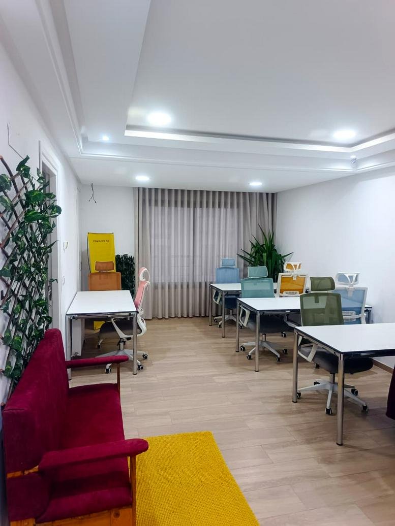 A shared office at Hive12, 65 شارع الجمهورية featuring several desks, colorful chairs, and a red sofa lounge area.