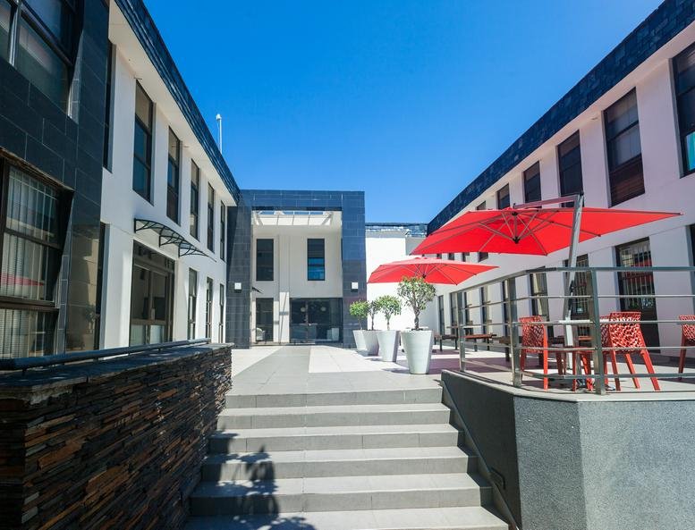 Exterior courtyard of Albury Office Park with white buildings, red umbrellas, and potted plants.