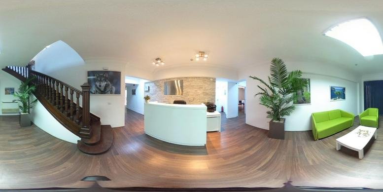 Modern reception lobby with curved white desk, wooden floors, and green seating area.