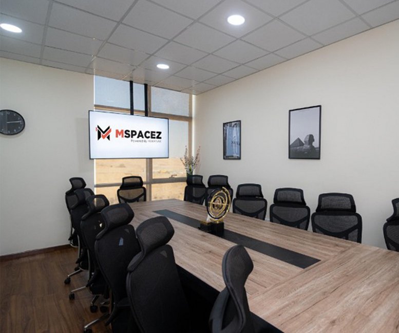 Spacious boardroom featuring a large wooden table, mesh chairs, and a wall-mounted screen.