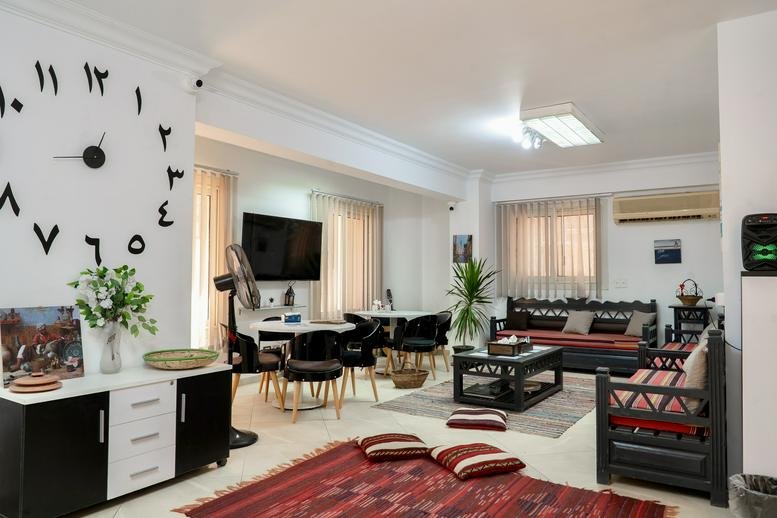 Spacious communal lounge with patterned rugs, traditional wooden seating, and a large wall clock with Arabic numerals.