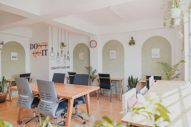 Spacious coworking area at Visara, Honey Pot Road, Rongai, with wooden tables, grey chairs, and indoor plants.