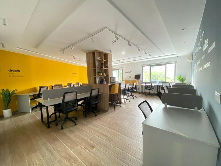 Spacious open-plan workspace at ZonAct Business Center featuring a vibrant yellow wall and modern white desks.