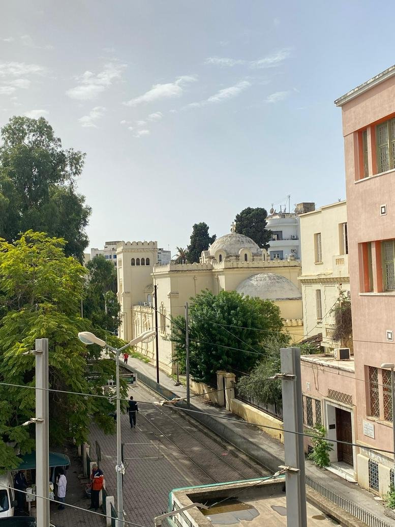 Exterior street view from a balcony overlooking traditional light-colored buildings.