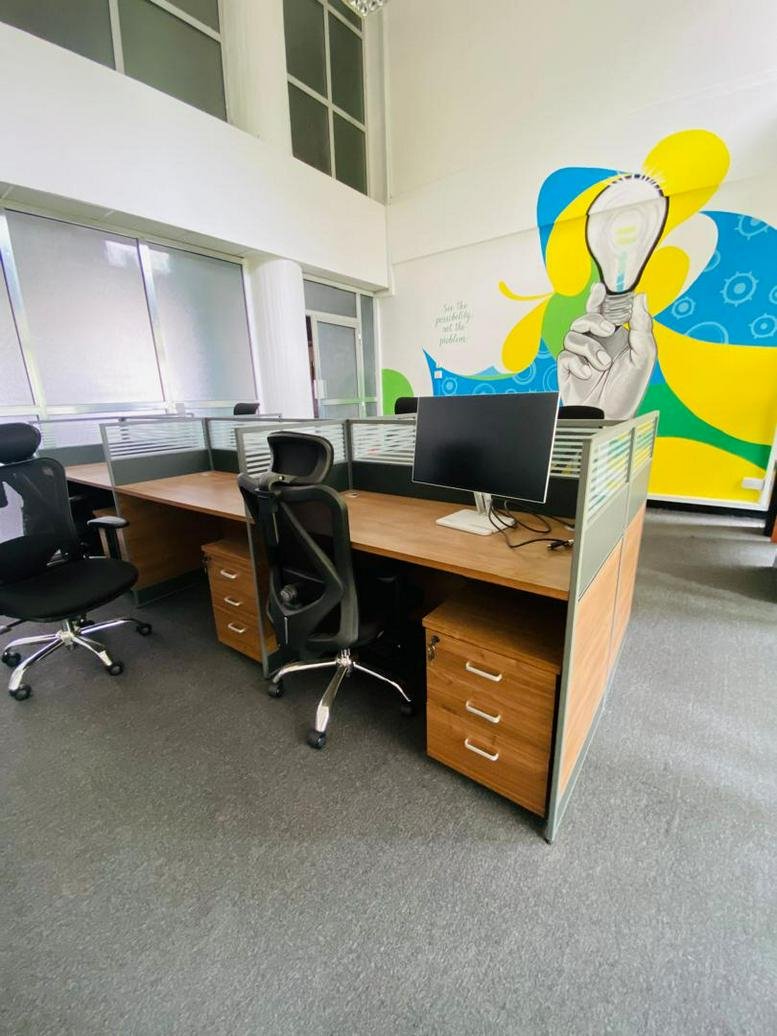 Bright workspace at NIC Investment House featuring wooden desks, ergonomic chairs, and a colorful lightbulb mural.