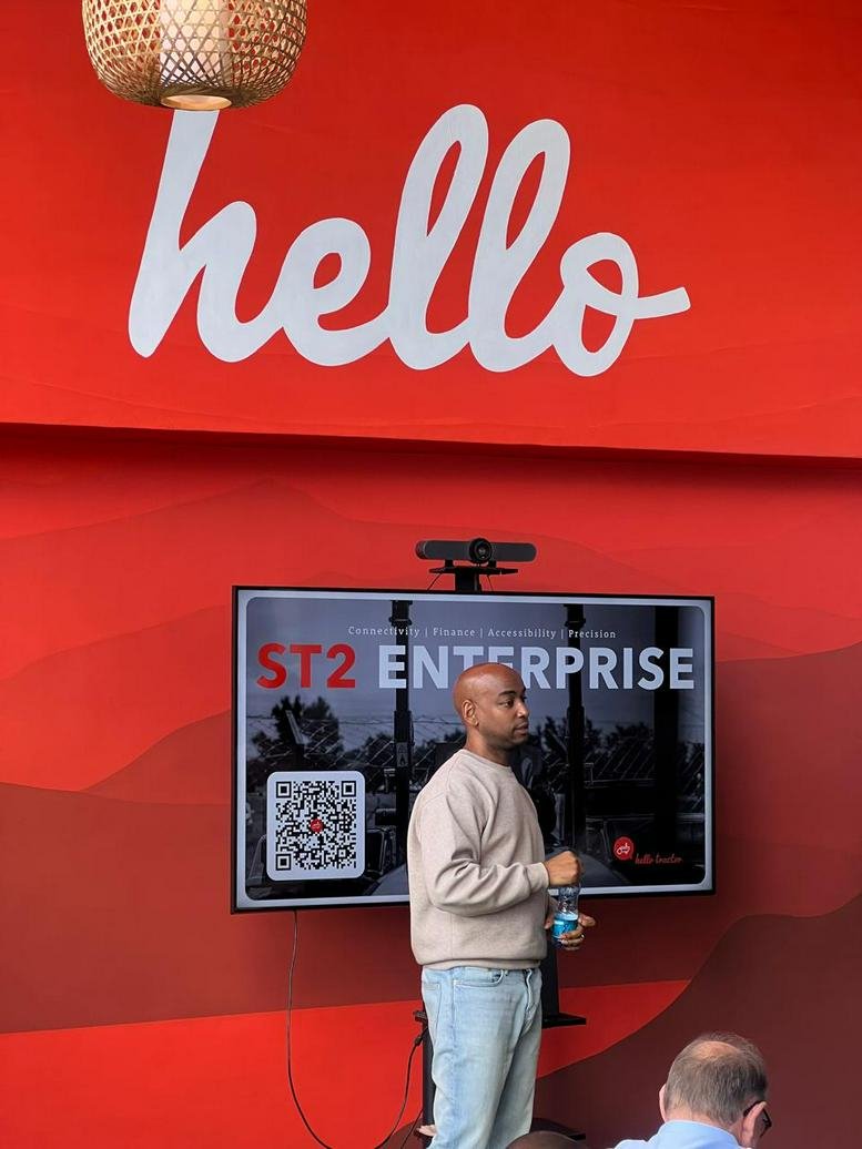 Presenter standing before a digital screen in a red branded event space.