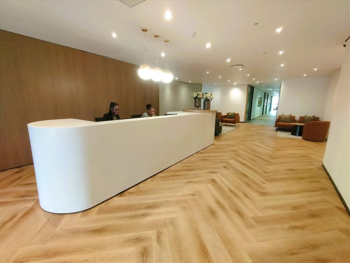 Bright reception area of West Tower at Nelson Mandela Square featuring a curved white desk and wood flooring.