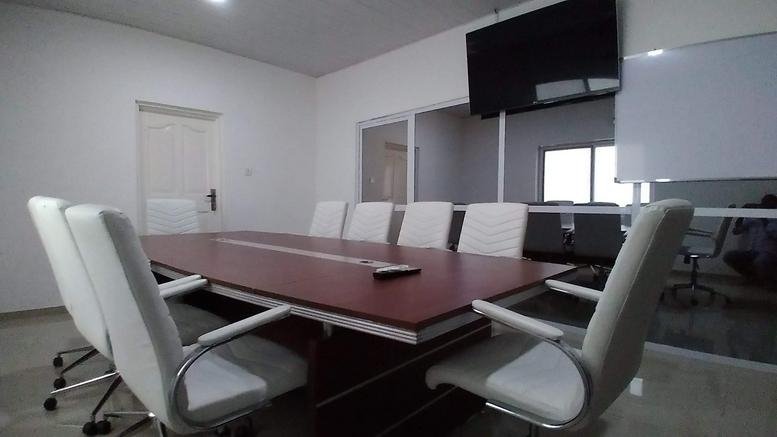 Spacious boardroom featuring a large wood-finish table and white executive chairs.