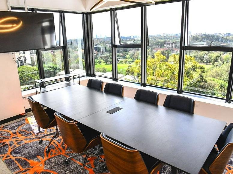Spacious boardroom with a dark table, wooden-backed chairs, and panoramic green views.